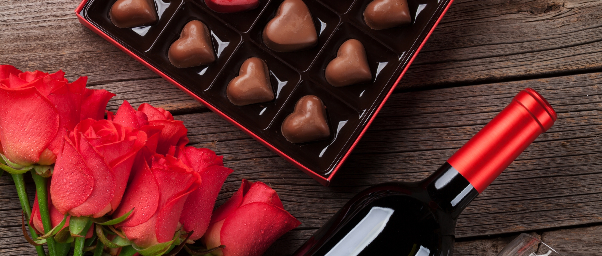 red roses, wine, and a box of chocolates laying on a table